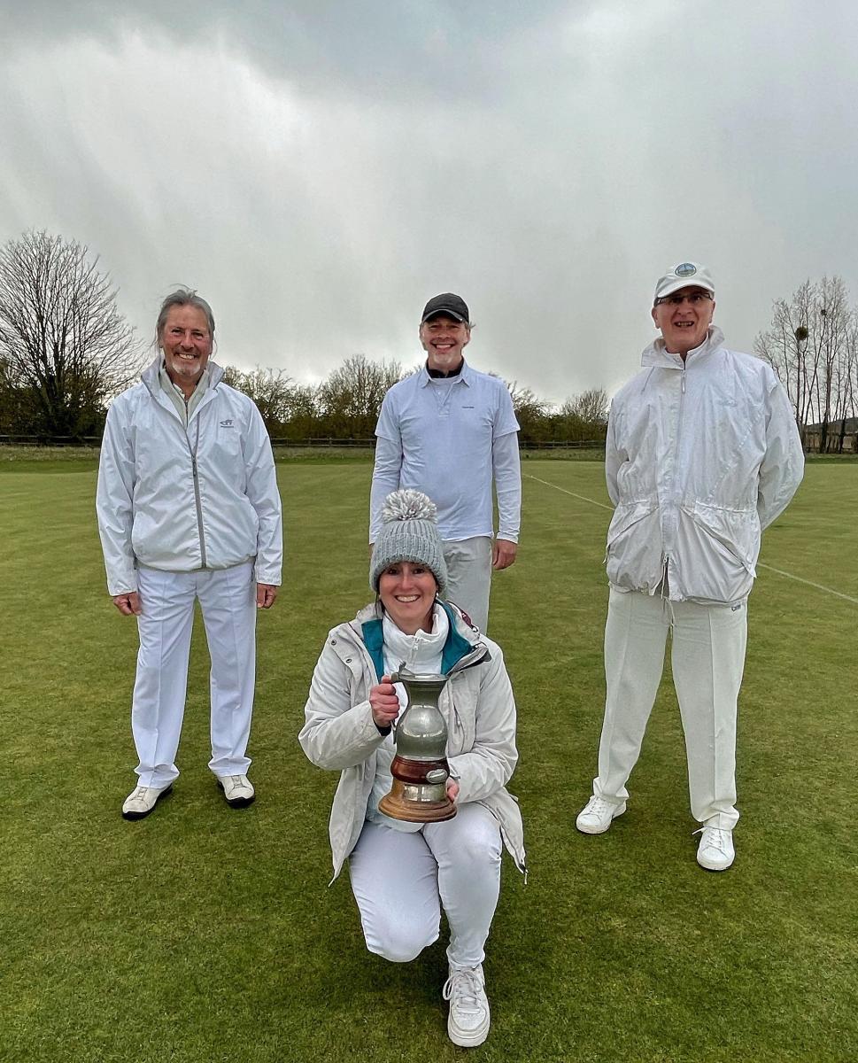 Four players dressed for the cold, under sultry skies, with Sophie kneeling at the front with a large silver trophy